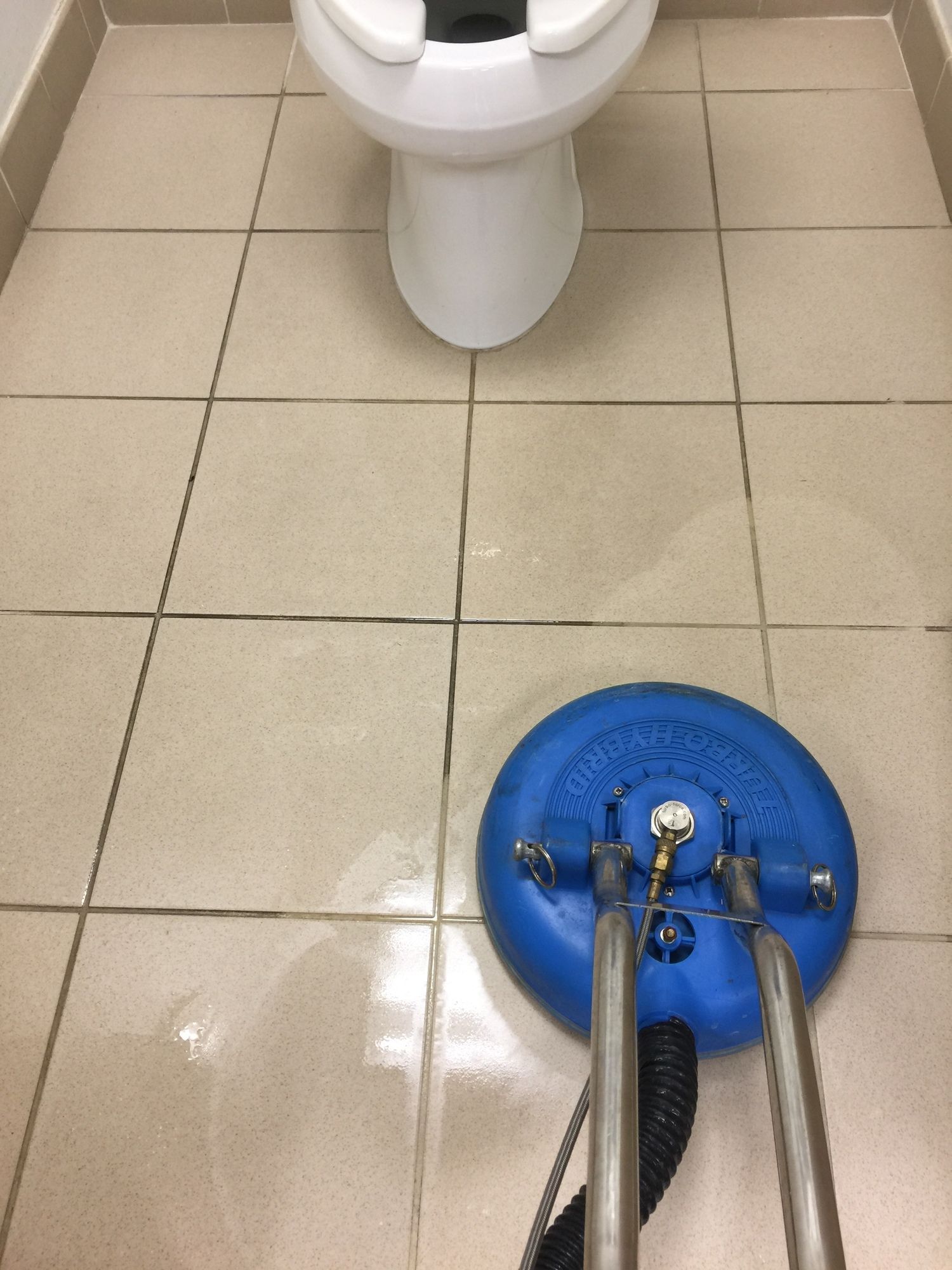 A blue vacuum cleaner is sitting on a tiled floor next to a toilet.