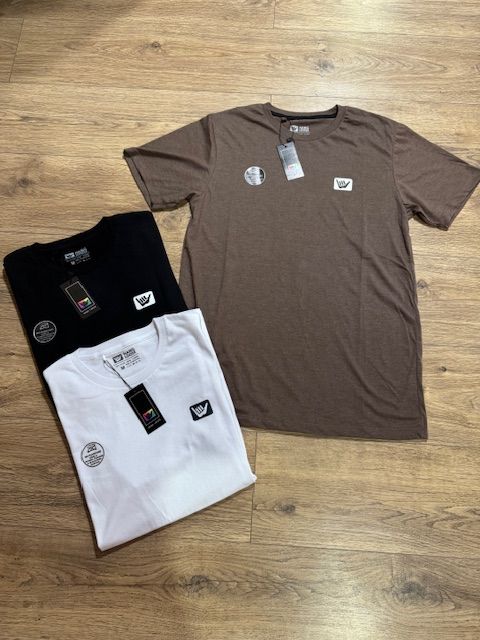 Tres camisetas están apiladas una encima de otra sobre un piso de madera.