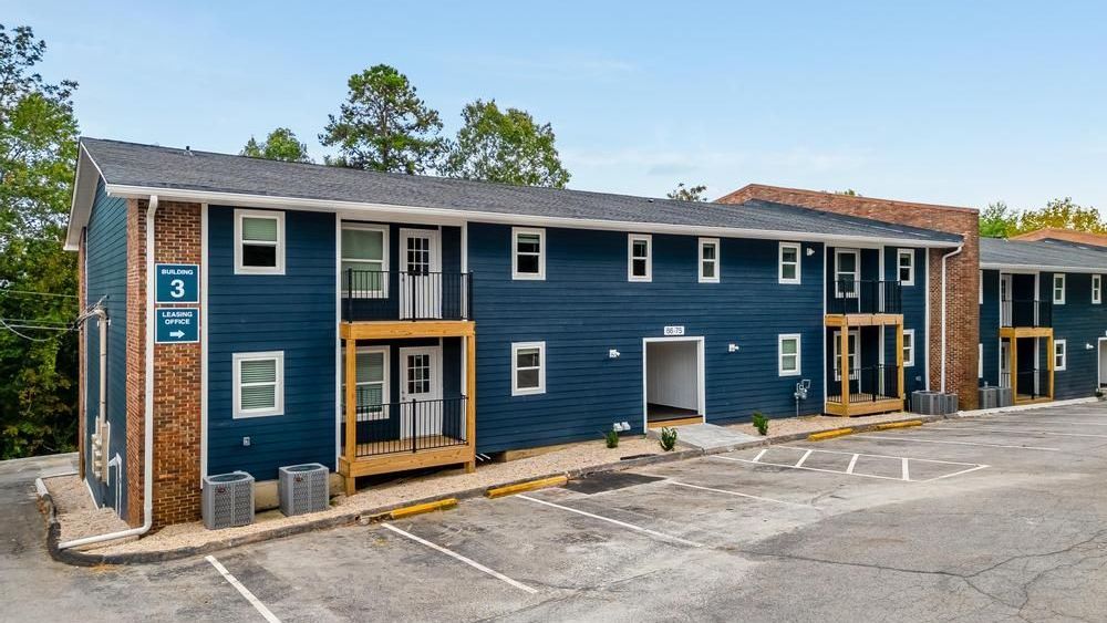 A blue apartment building with a parking lot in front of it.