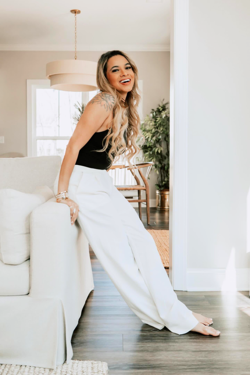 A woman is leaning on a white couch in a living room.