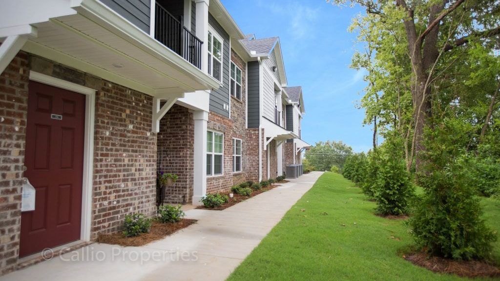 A brick apartment building with a red door and a walkway leading to it.