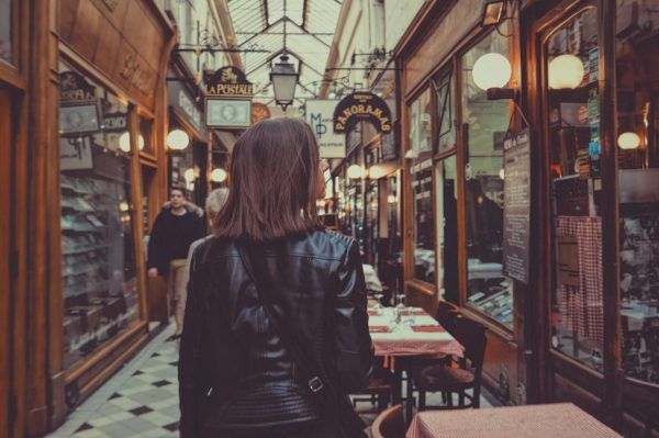 A woman is walking through a narrow alleyway filled with tables and chairs.