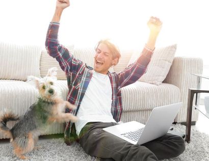 A man is sitting on the floor with a laptop and a dog.