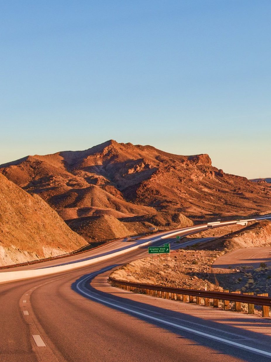 Highway curves through a desert landscape with brown mountains under a blue sky.