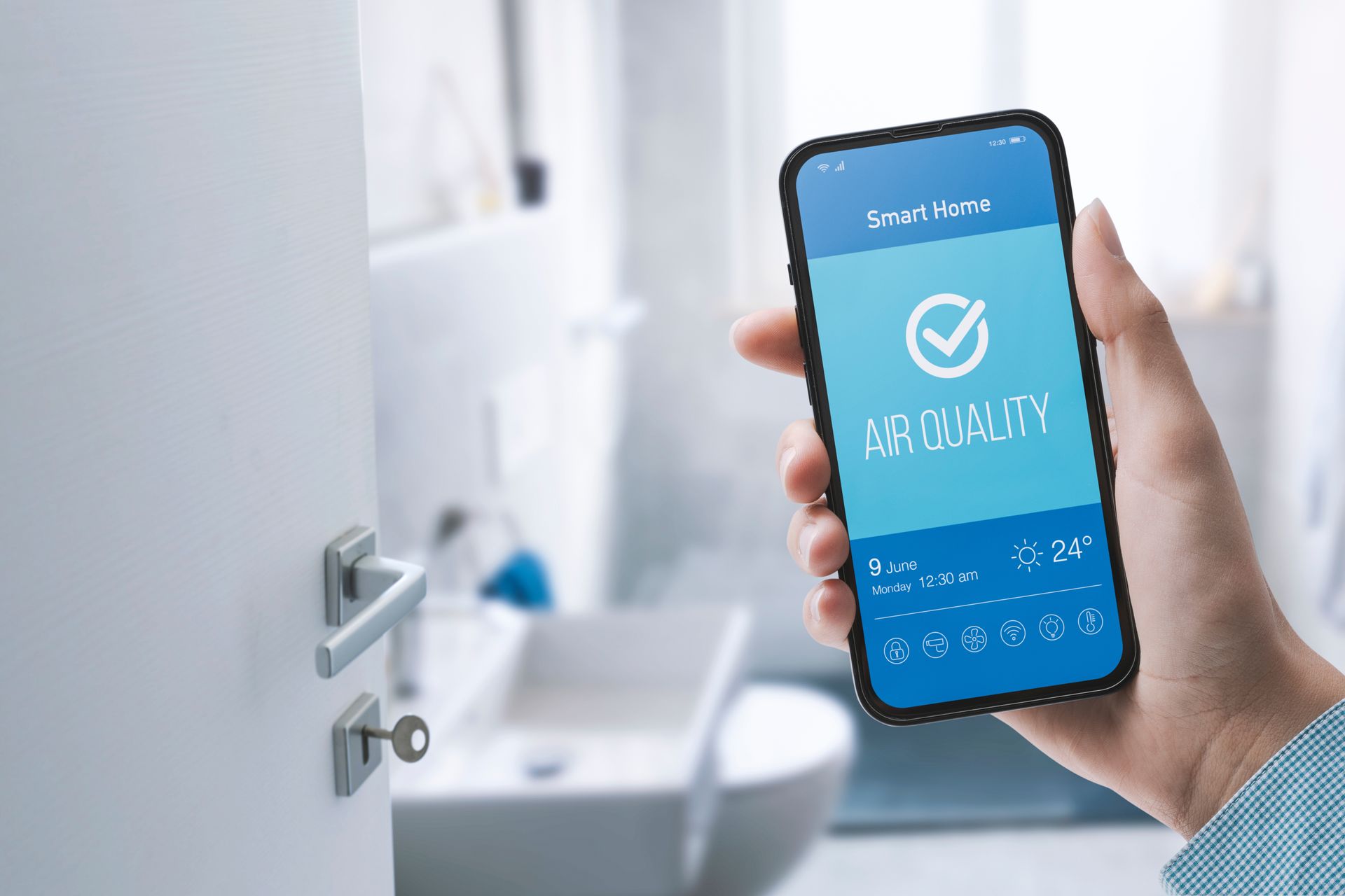 Hand holding phone displaying air quality app in a bathroom. App shows a checkmark indicating good air quality.