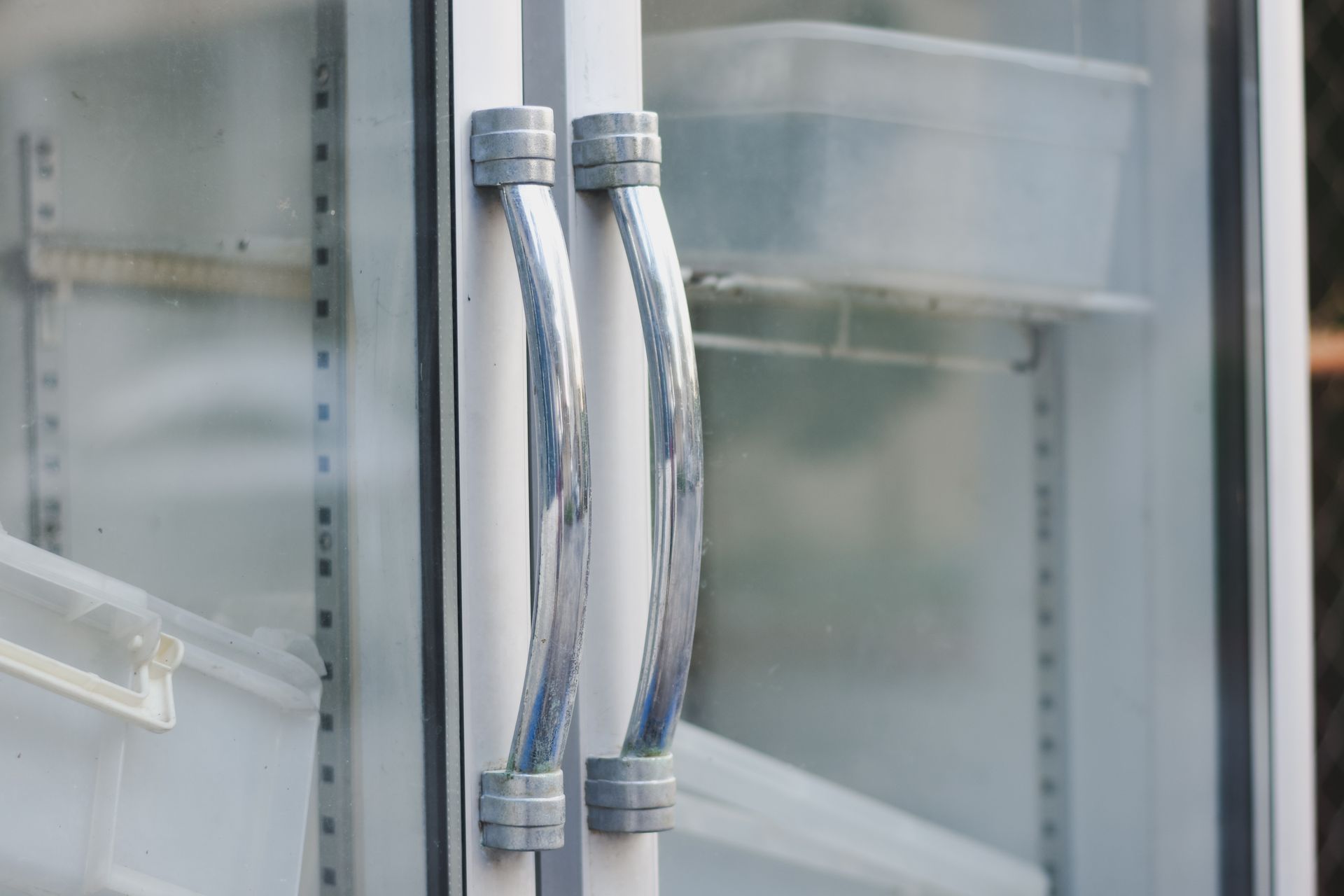 White, glass-doored refrigerator with curved silver handles. Empty shelves inside.