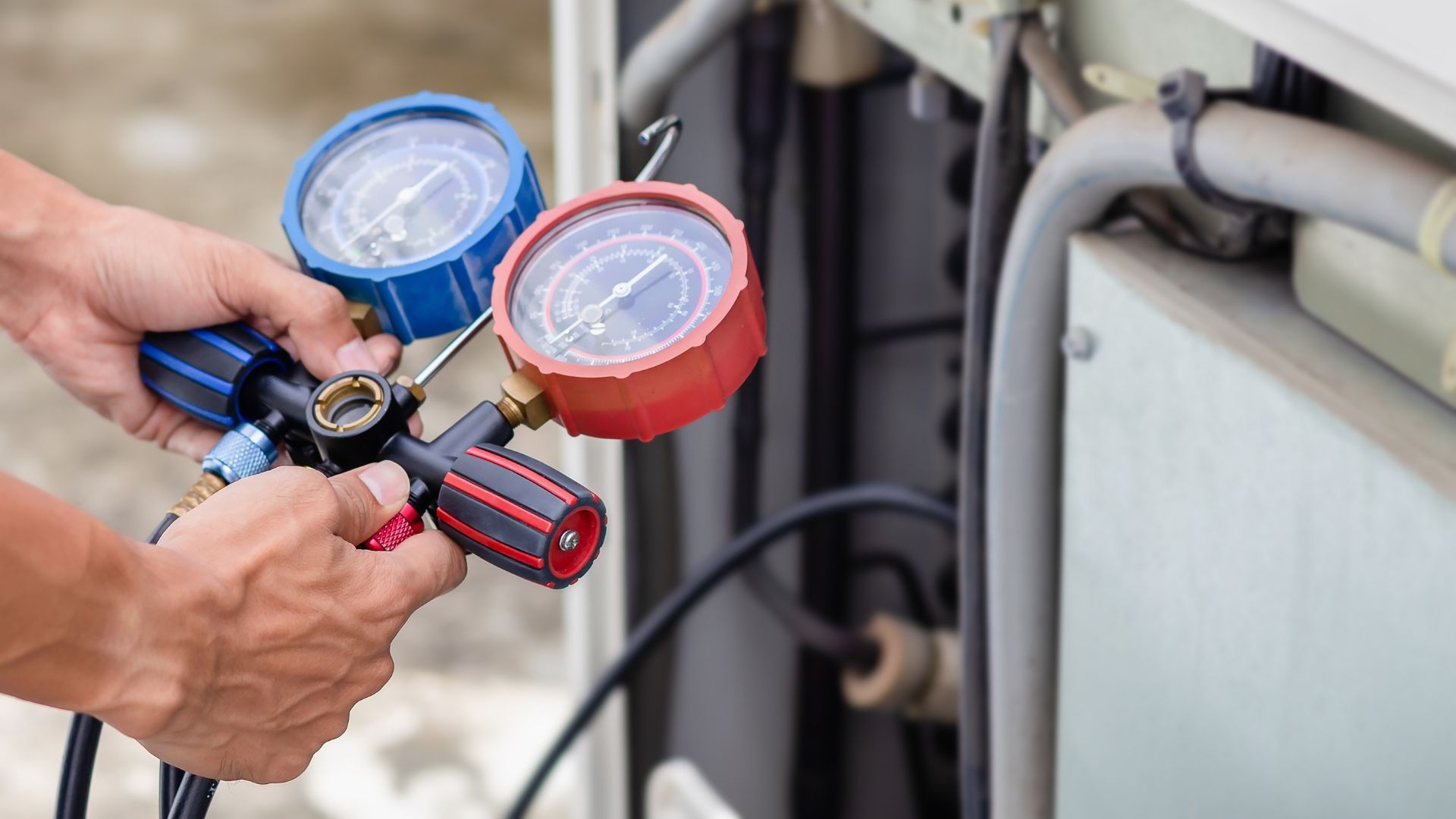 A man is working on an air conditioner with a screwdriver and gauges.