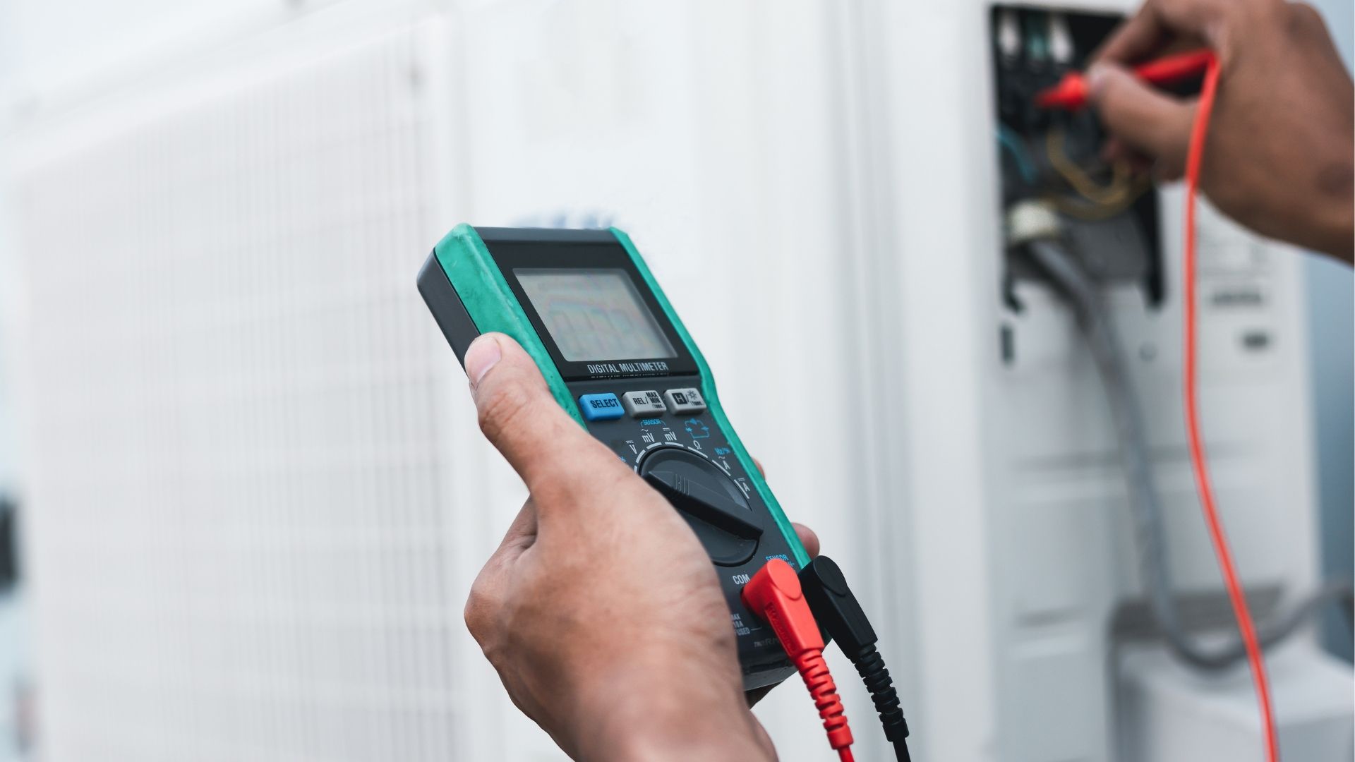 A person is holding a digital multimeter in their hand.