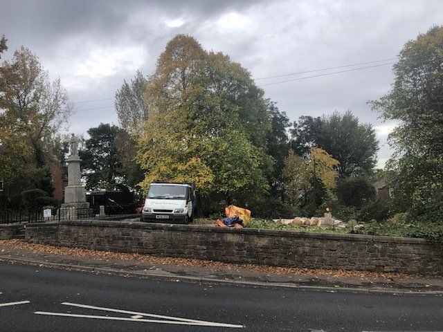 A white van is parked on the side of the road next to a stone wall.