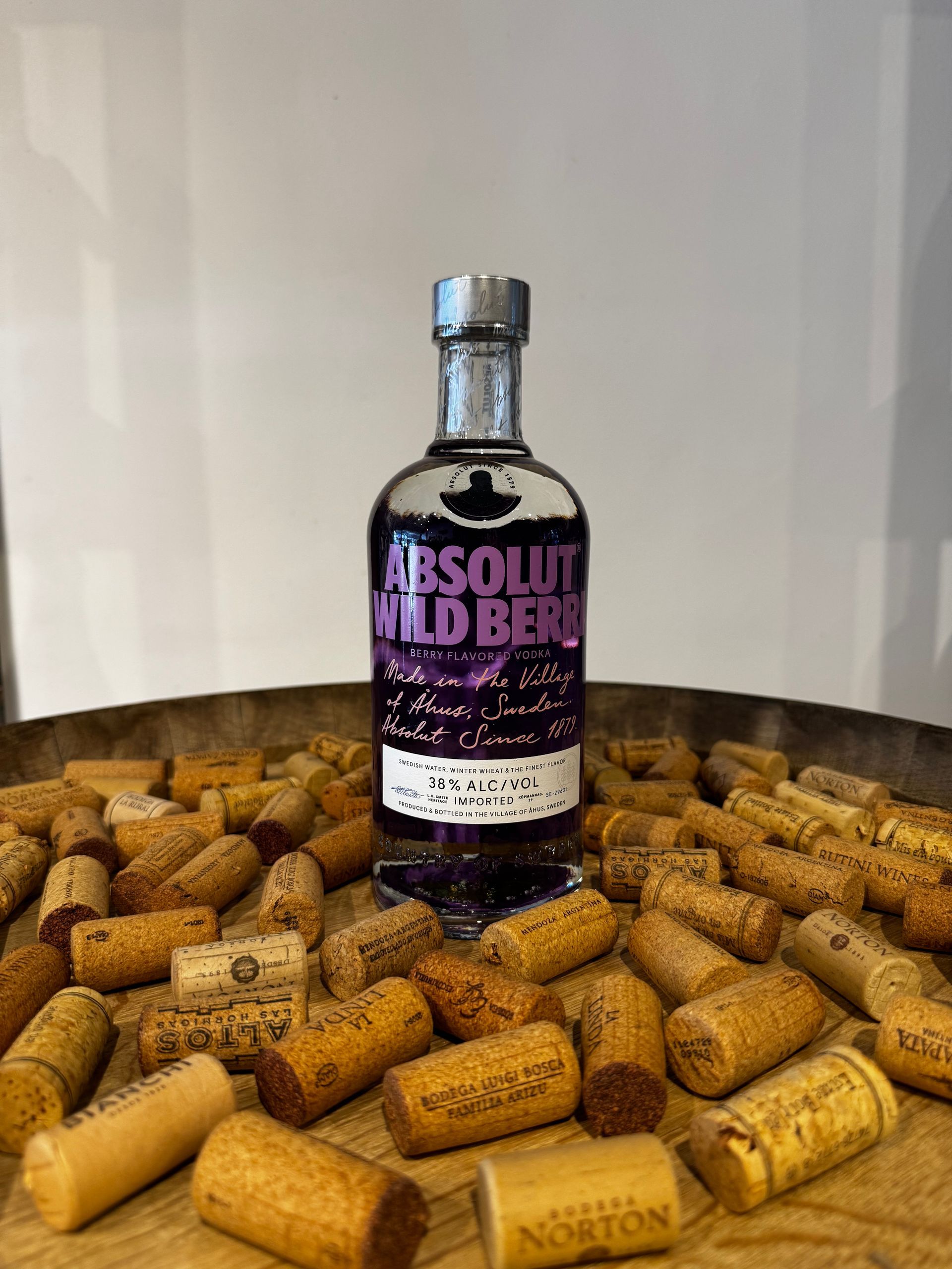Botella de vodka Absolut Wild Berri sobre un fondo de corchos de vino. Etiqueta morada, tapón plateado y fondo de madera.
