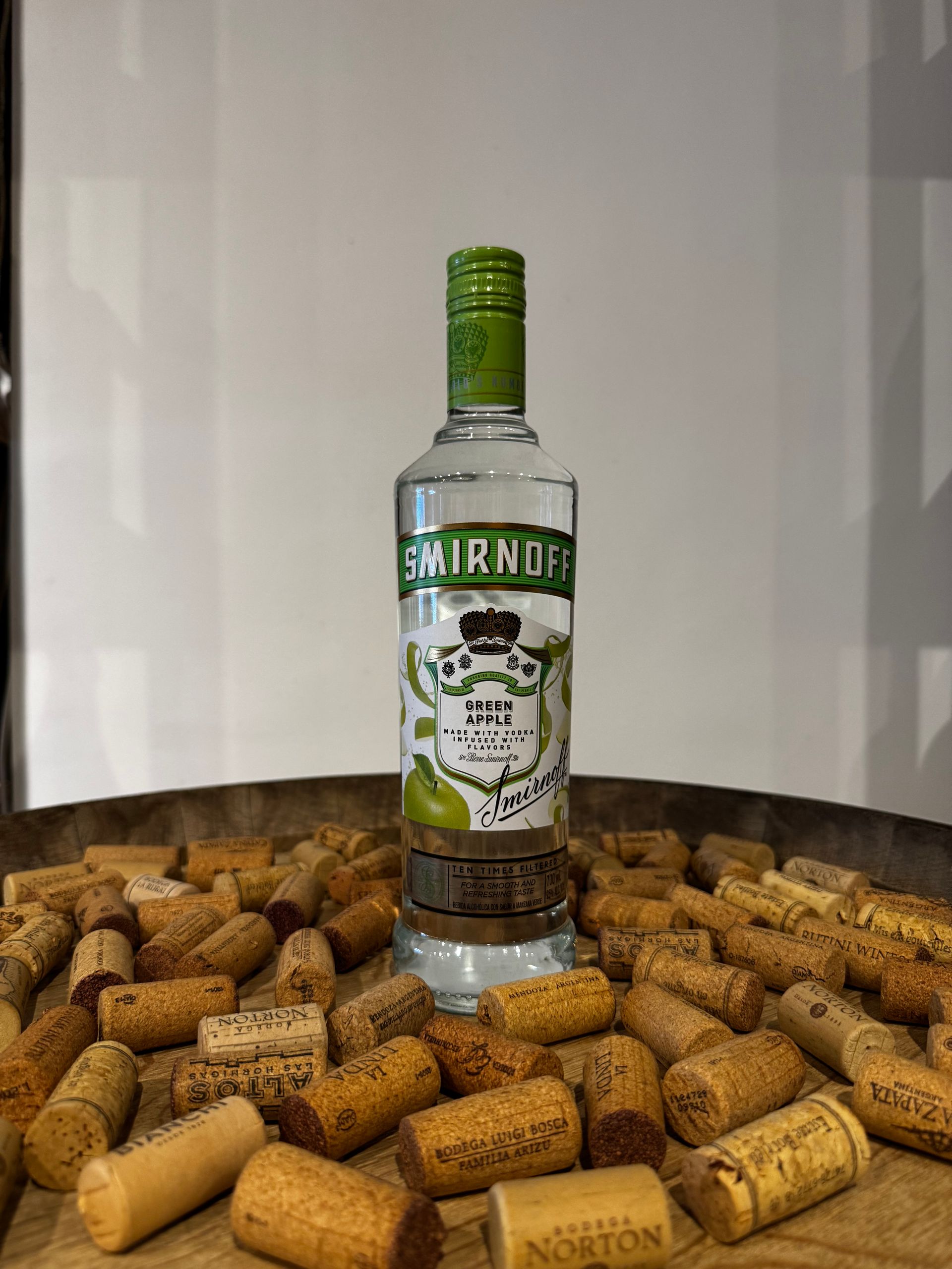 Botella de vodka Smirnoff TAG con etiqueta de lima, sobre un lecho de corchos dispersos.