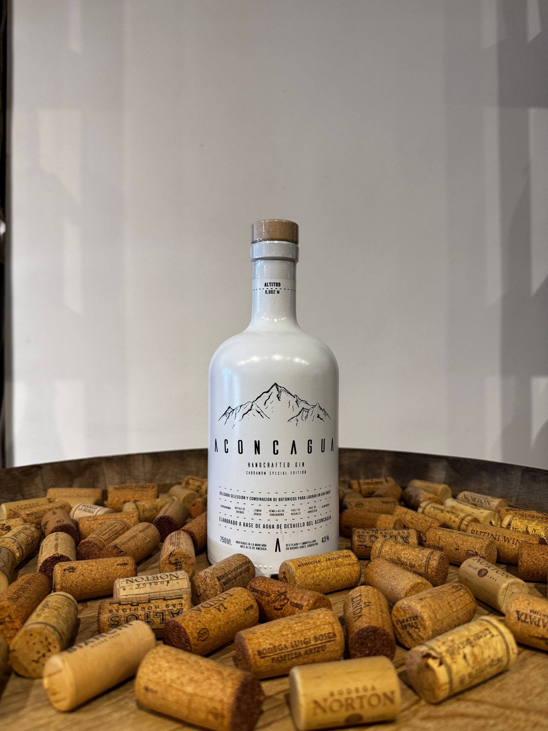 Botella de vino blanca con gráfico de montaña, rodeada de corchos.