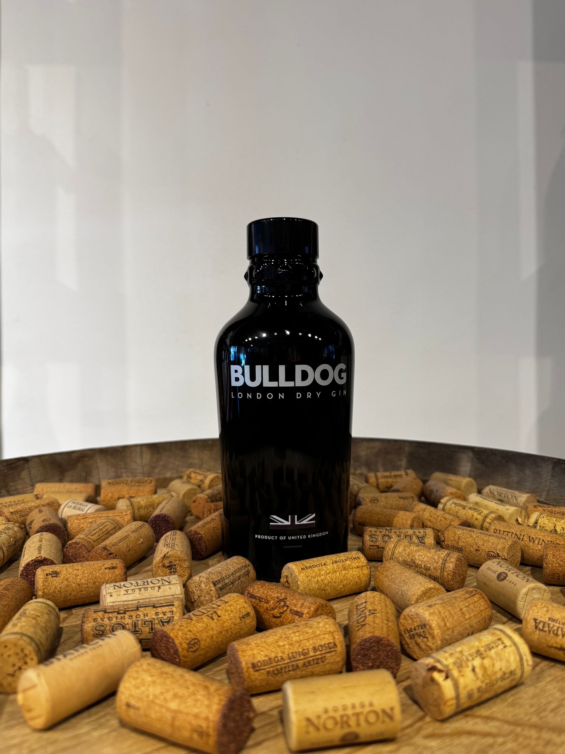 Botella de ginebra Black Bulldog rodeada de corchos dispersos sobre una superficie de madera.