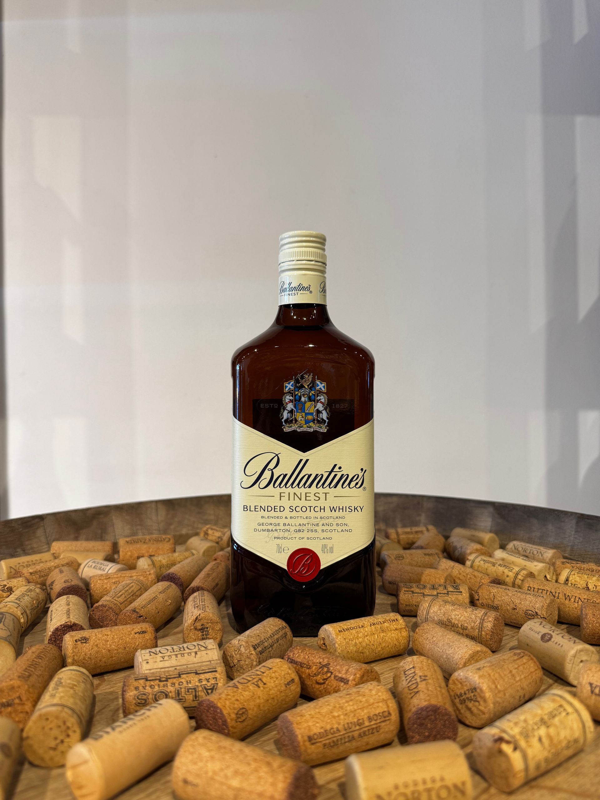 Botella de whisky escocés Ballantine's sobre un lecho de corchos, sobre un fondo neutro.