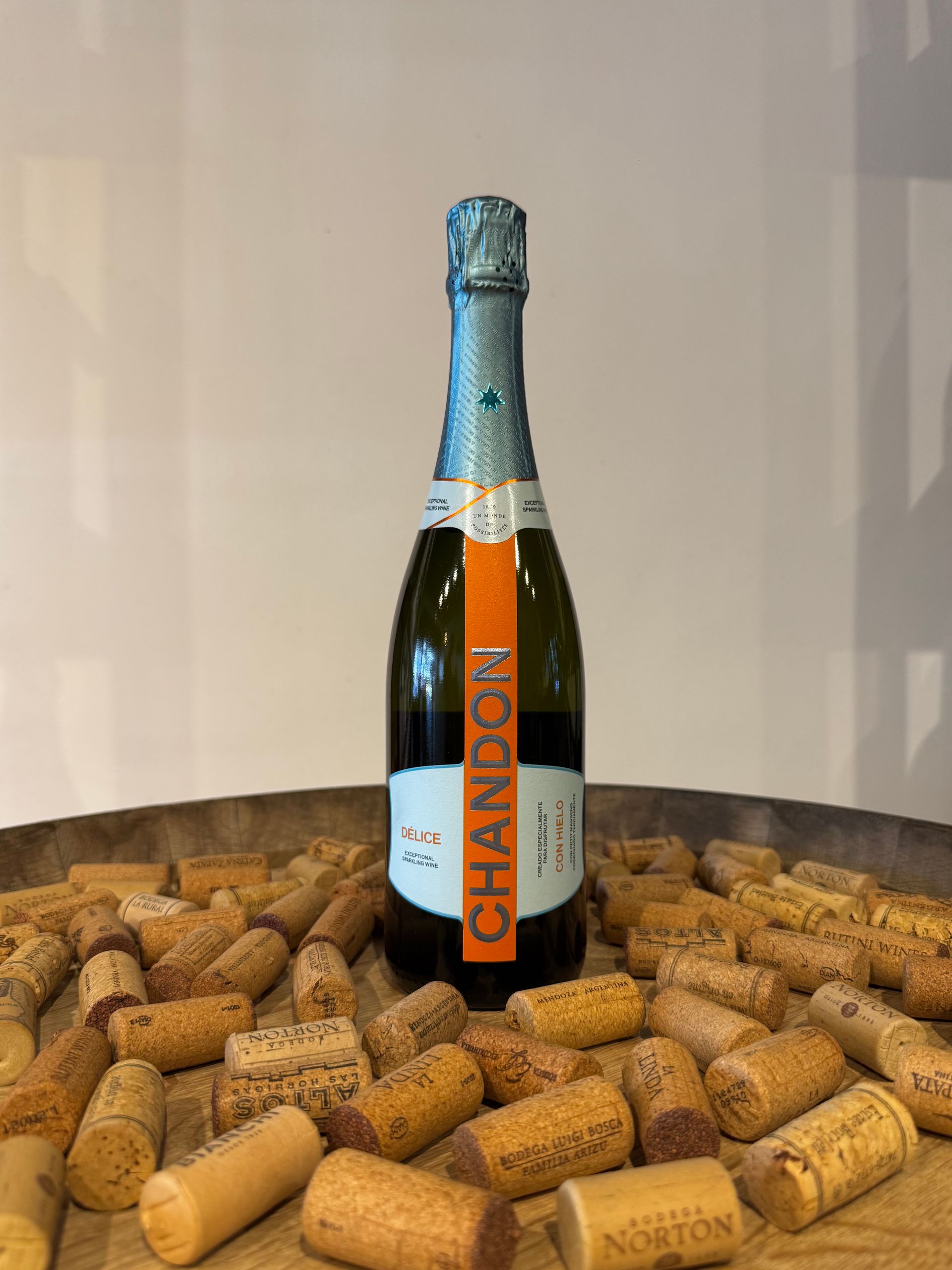 Botella de vino espumoso Chandon sobre un lecho de corchos; etiqueta naranja, papel de aluminio verde azulado.
