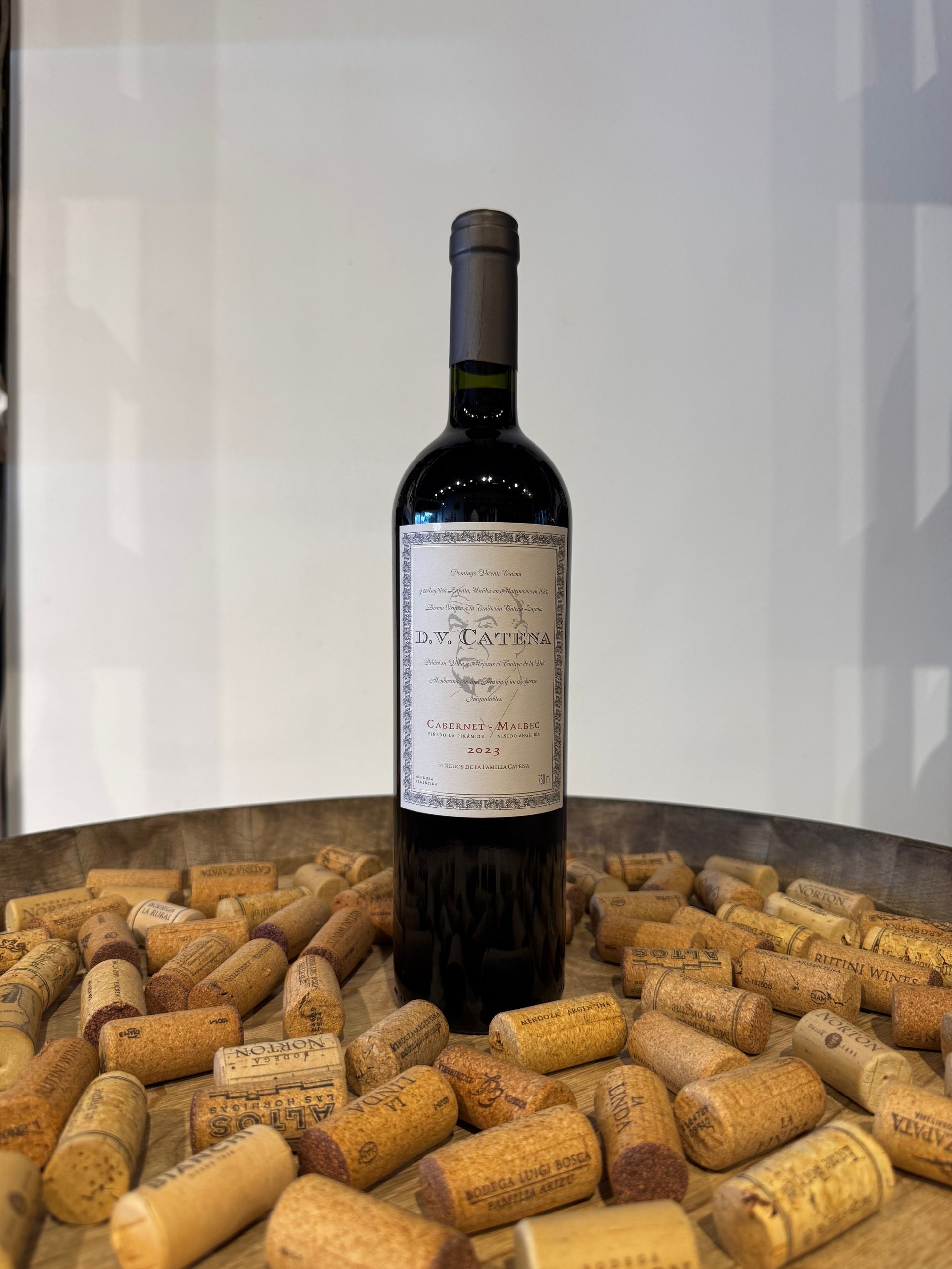 Botella de vino sobre corcho, con etiqueta blanca, colocada sobre una superficie de madera, fondo blanco.