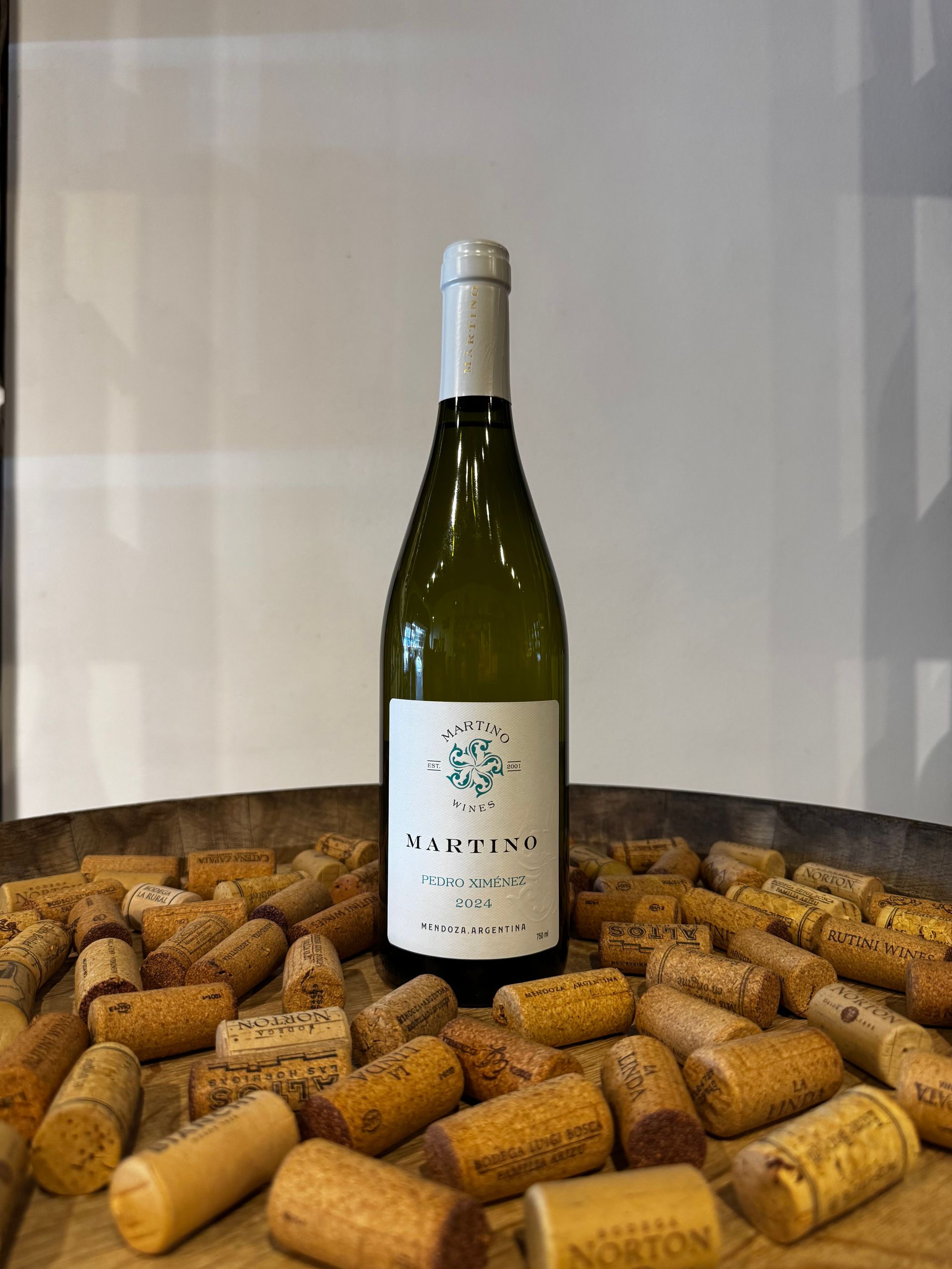 Botella de vino blanco con etiqueta verde, rodeada de corchos.