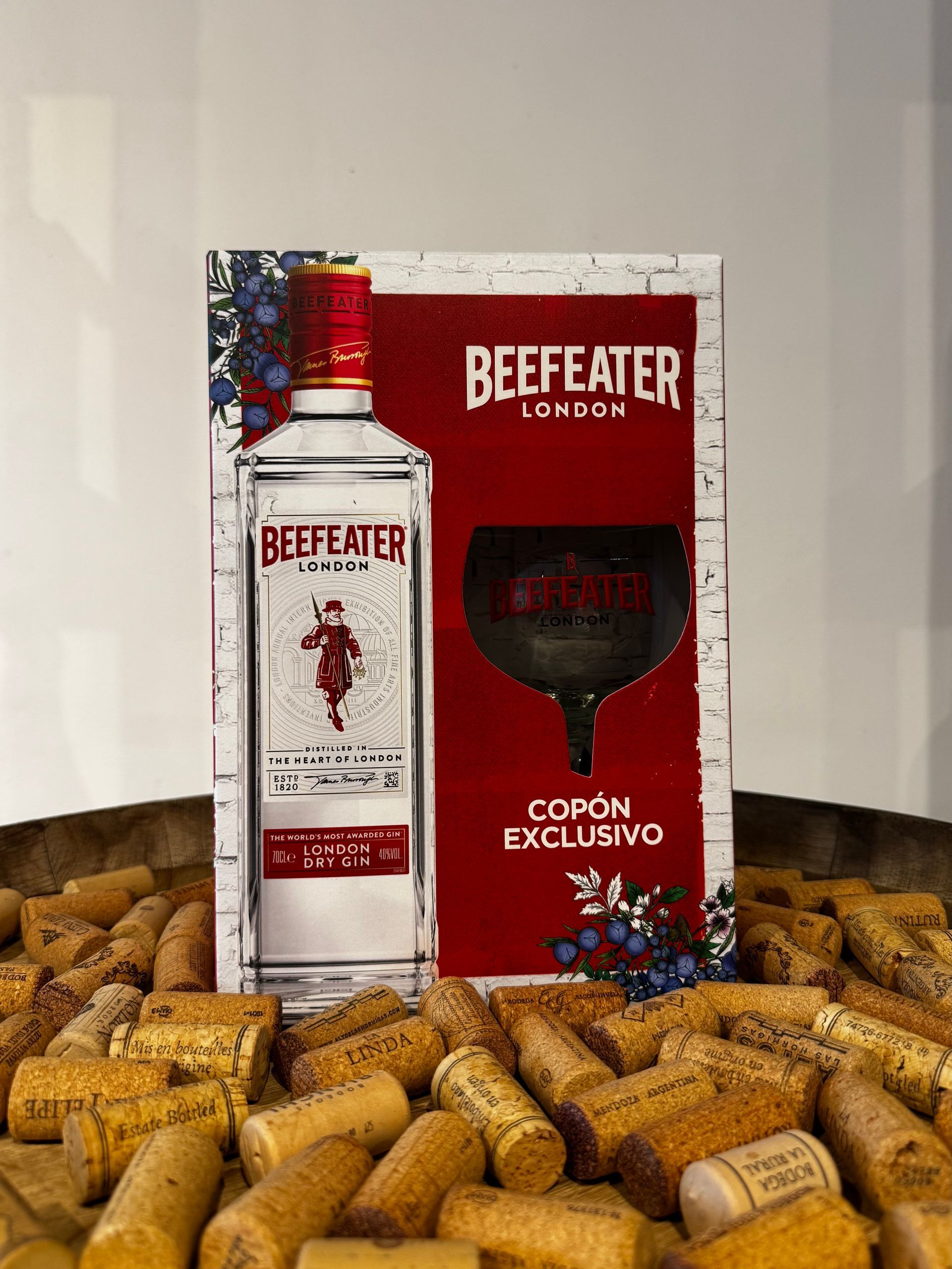 Botella de ginebra Beefeater y vaso de marca en un expositor promocional, rodeado de corchos.