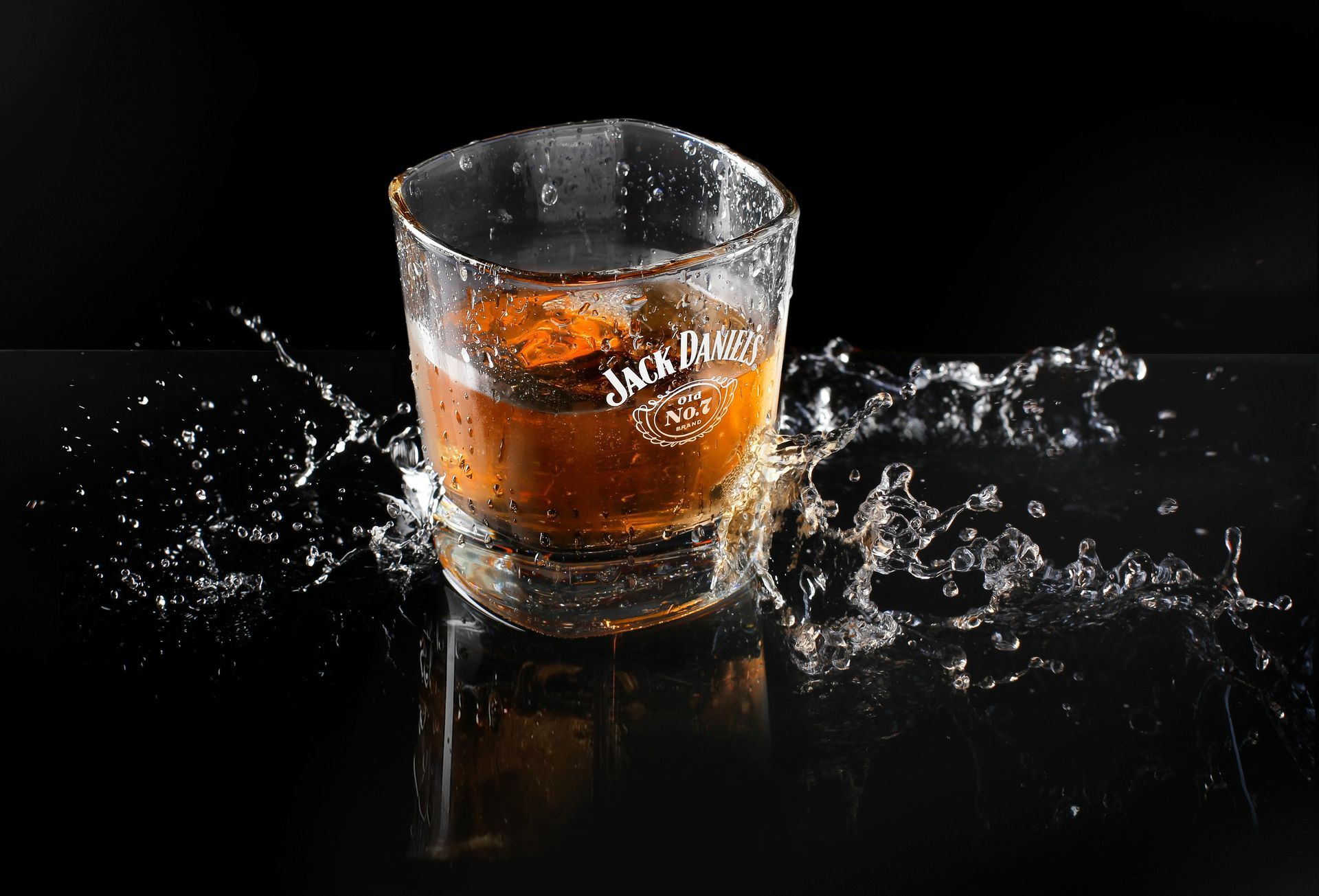 Vaso de whisky con el logo de Jack Daniel's, hielo, salpicaduras sobre un fondo negro.