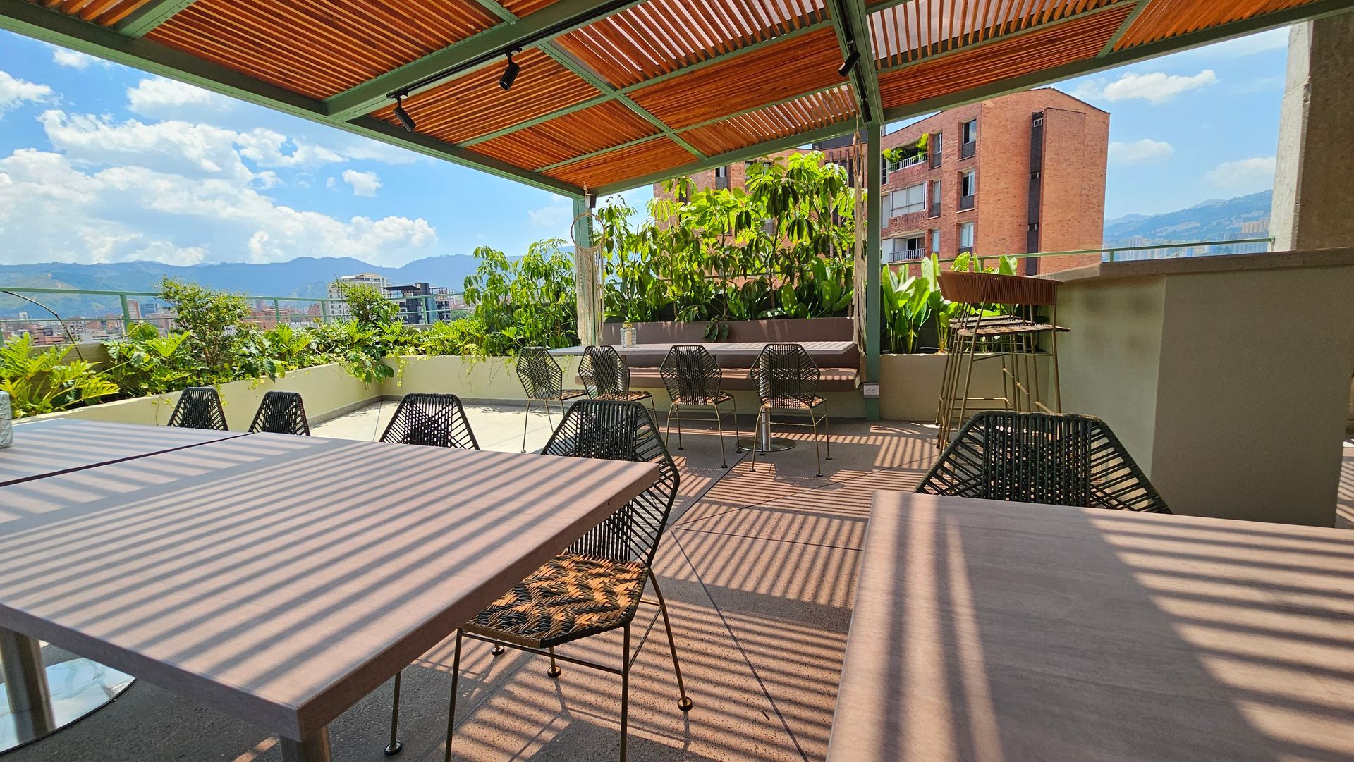 A patio with tables and chairs under a pergola on a sunny day.