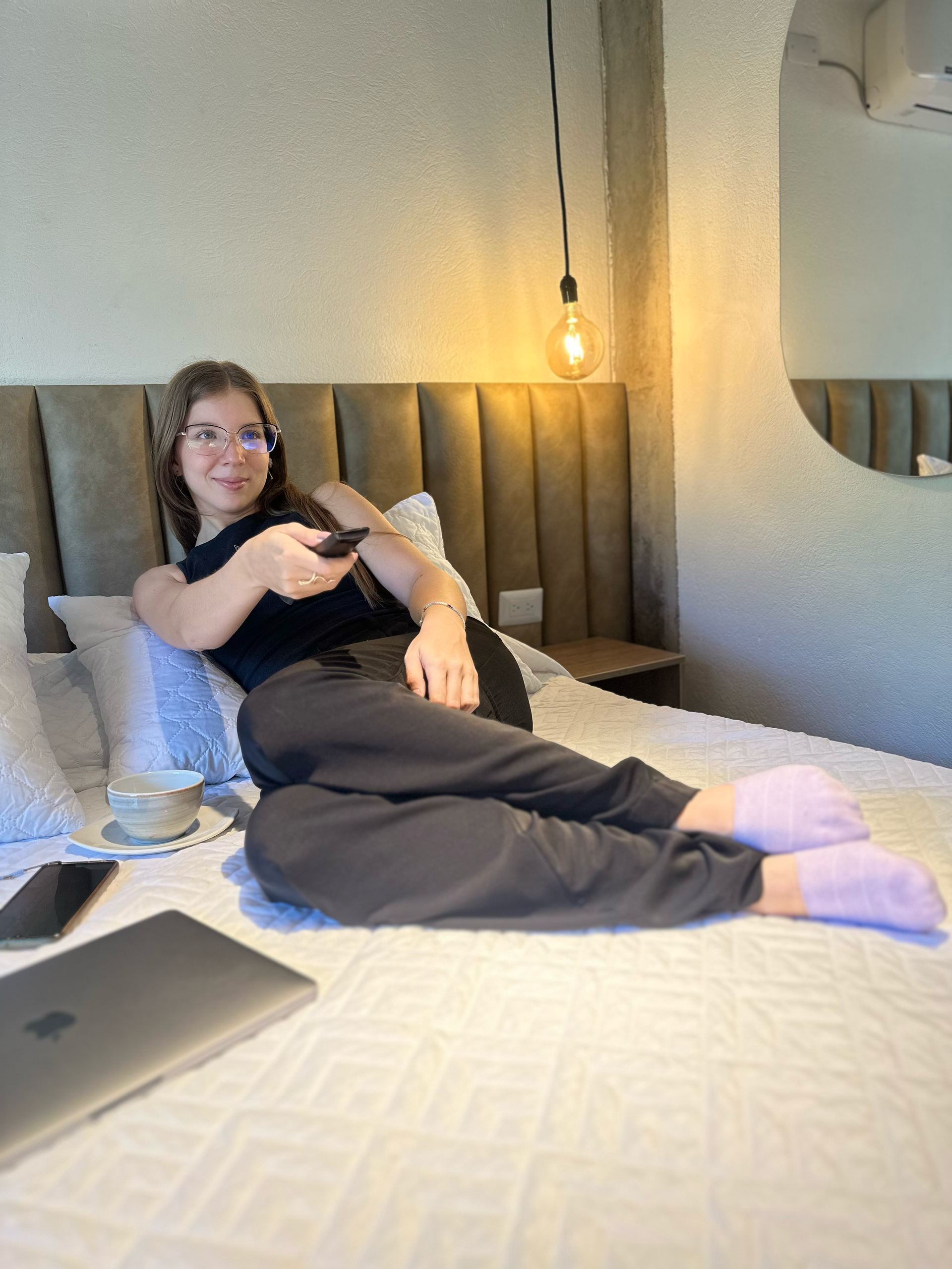 A woman is laying on a bed holding a remote control.