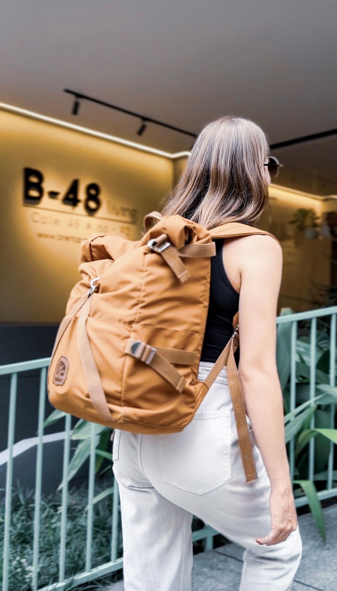 A woman wearing a brown backpack is standing in front of a building.