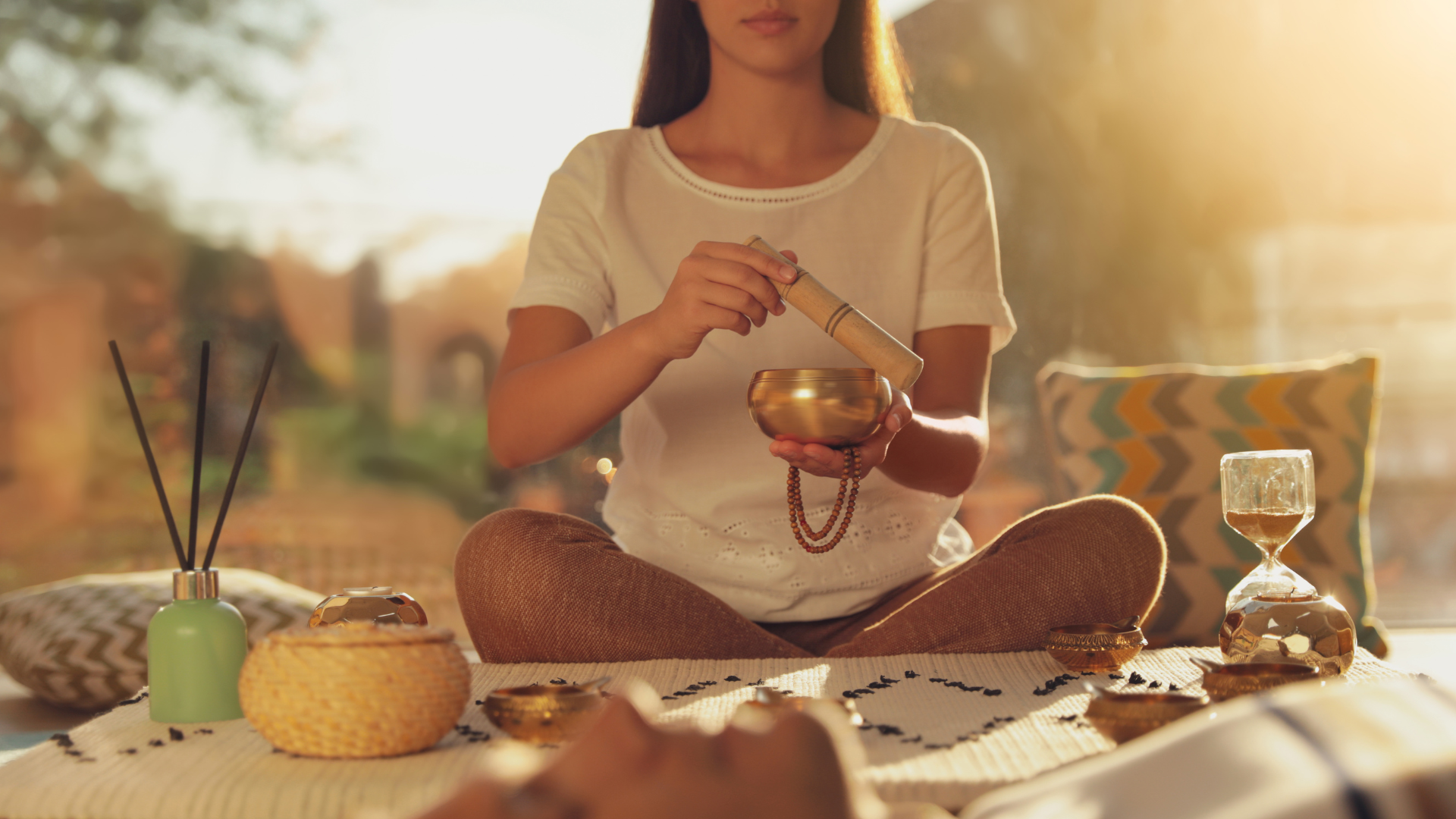 Una mujer está sentada en posición de loto sosteniendo un cuenco cantor.