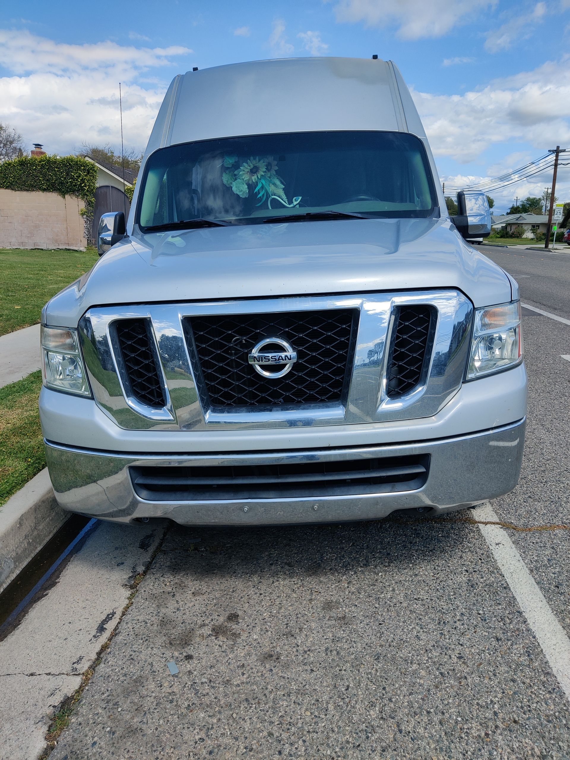 Silver Nissan NV high-roof cargo van parked on the side of a road.