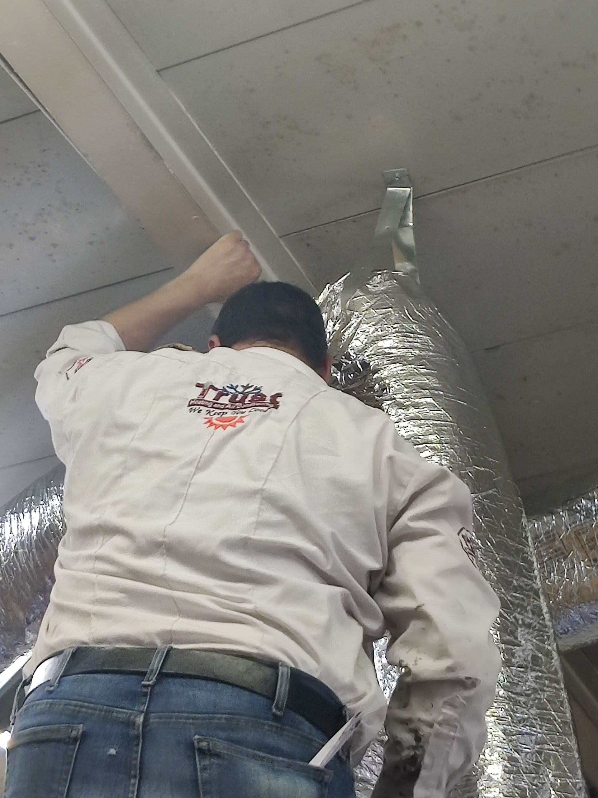 Person in work clothes installing foil ductwork in a ceiling.
