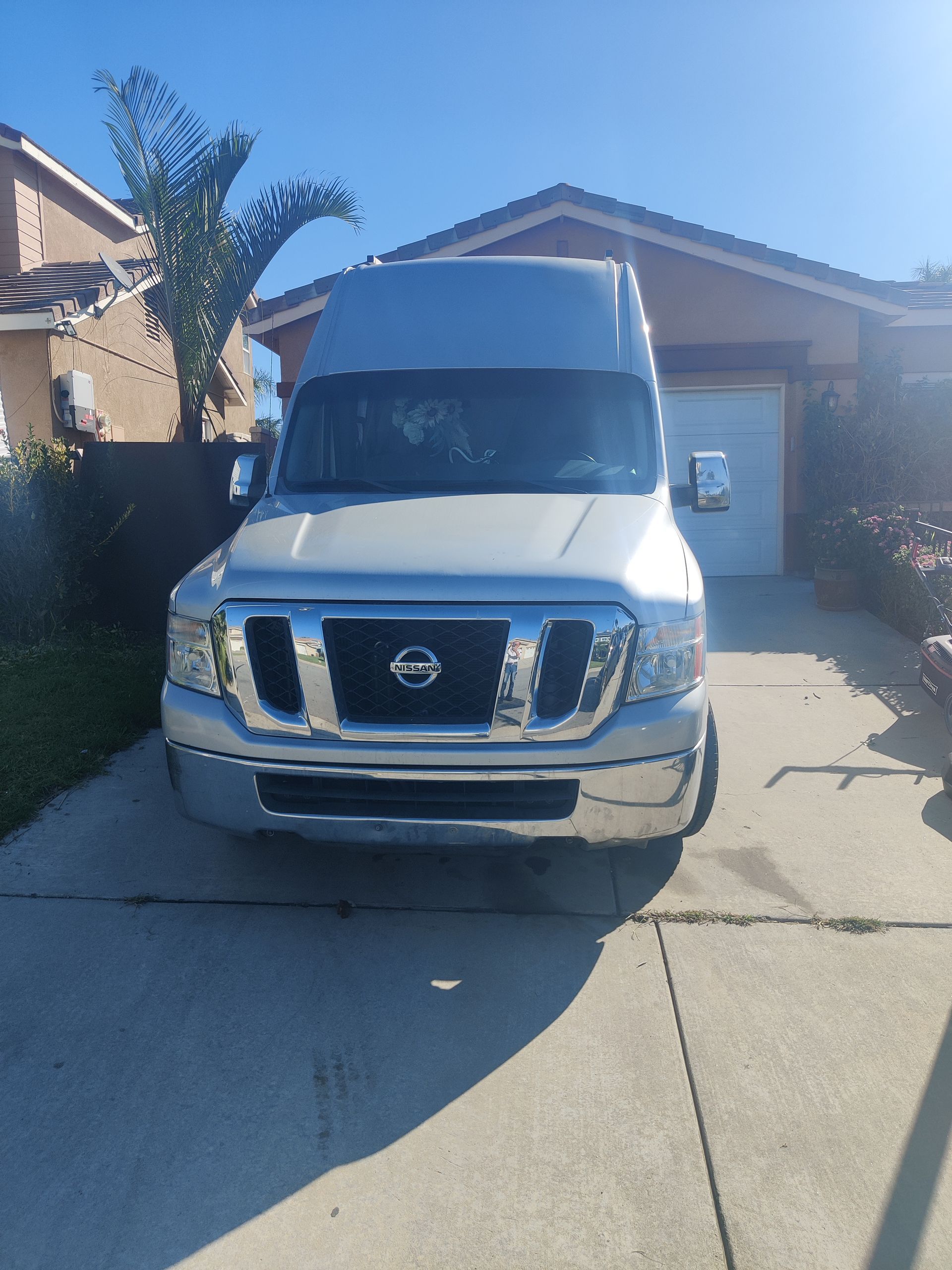 Silver Nissan van parked in a driveway in front of a house on a sunny day.
