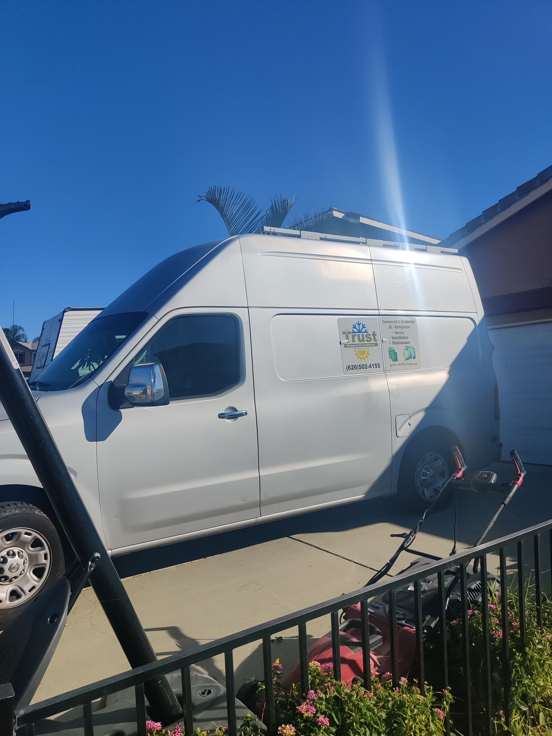 White van parked on a driveway with roof rack, under a bright blue sky.