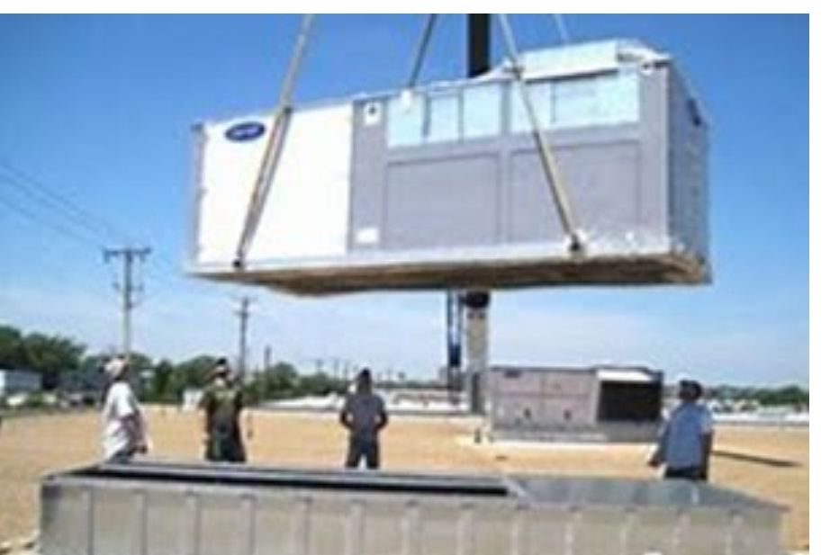 Crane lifting large HVAC unit onto a rooftop, with several workers observing on a sunny day.