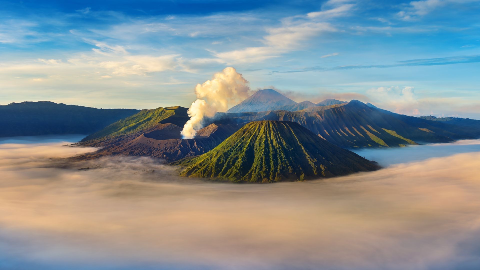 Volcanoes emerging from a sea of clouds under a blue sky, one with visible steam.