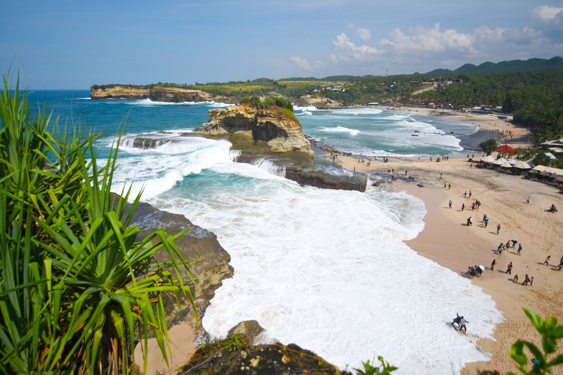 Beach with foamy waves, cliffs, and people on the sand under a sunny sky.