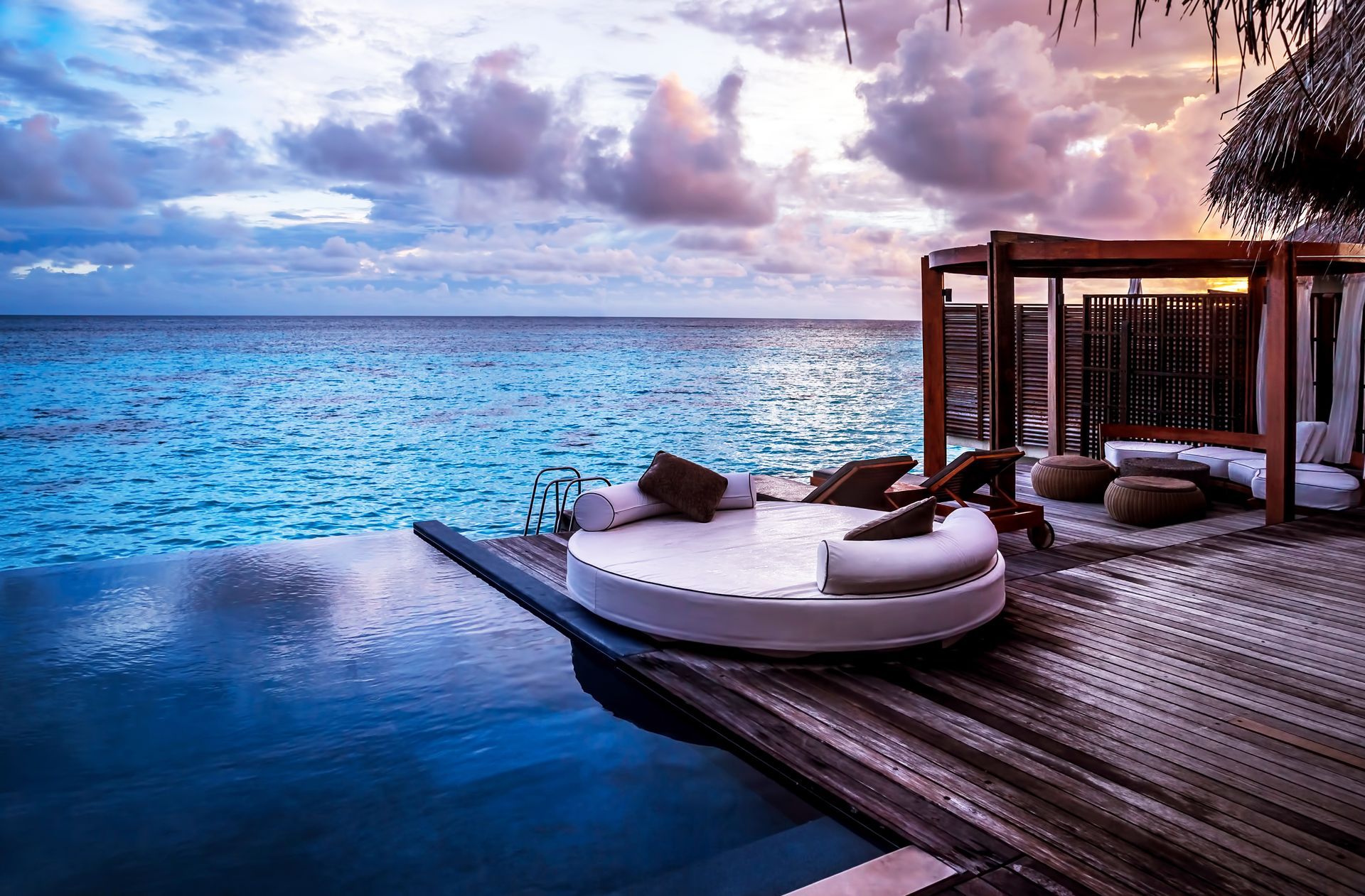 Infinity pool and lounge area with ocean view at sunset.