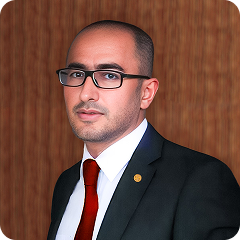 Man in suit and glasses looking at the camera against a wood-paneled background.