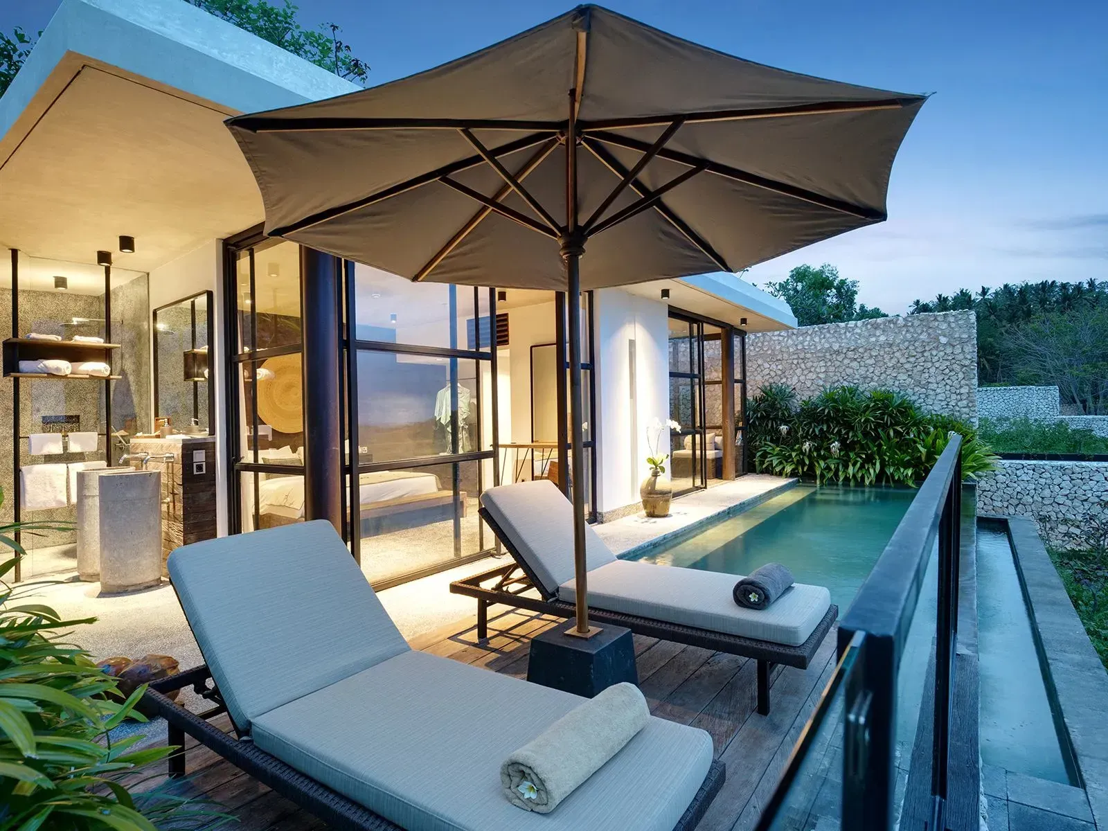 Lounge chairs under an umbrella by a small pool, overlooking a tropical landscape.