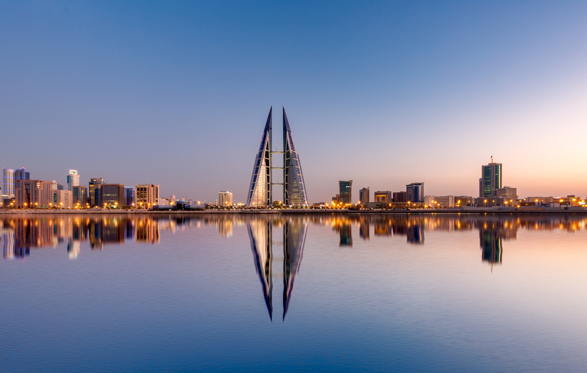 Twin towers reflected in water, part of a skyline at dusk, Bahrain.