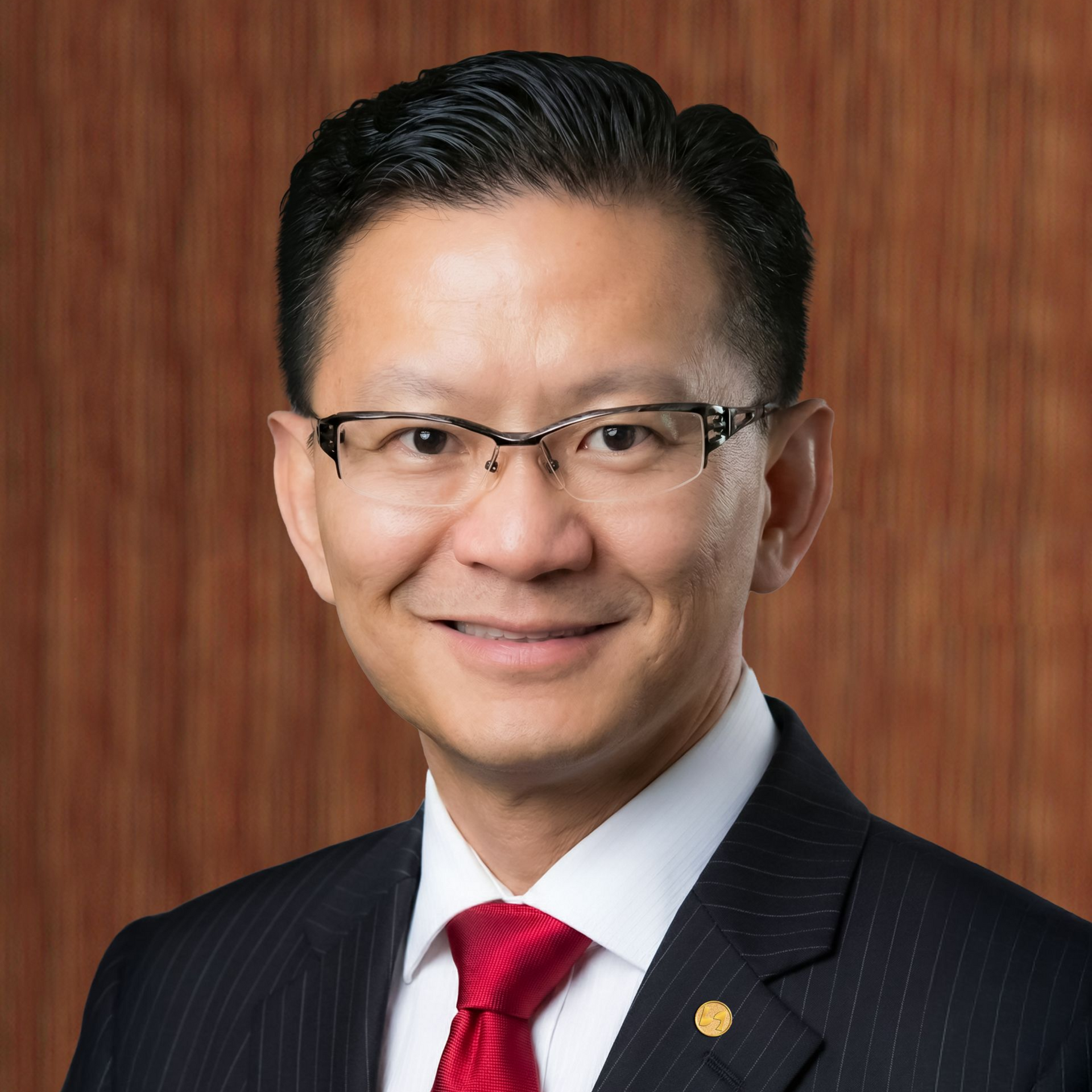 Man in a blue suit with a red tie smiles, set against a wooden background.