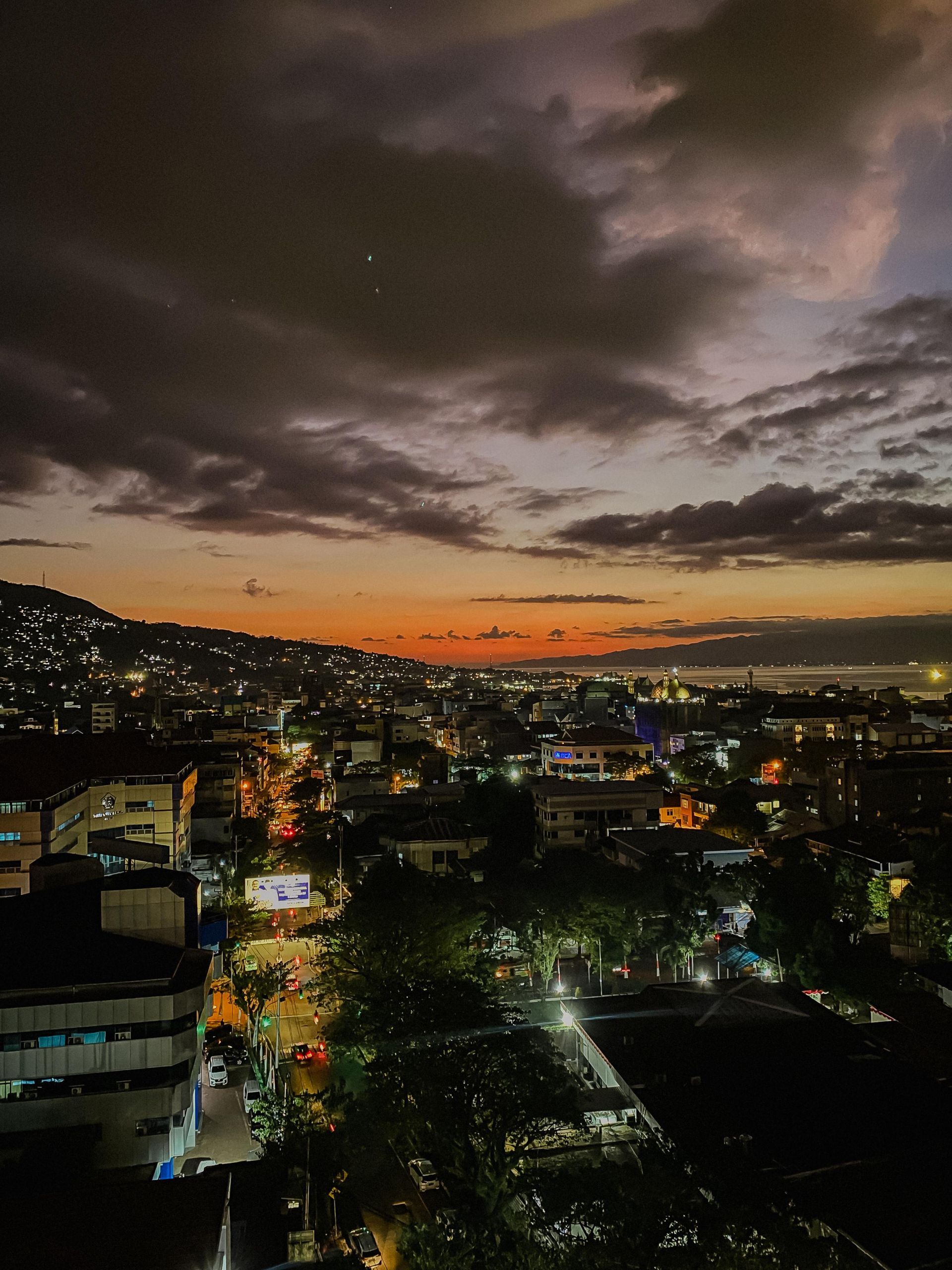 City skyline at dusk with lights, orange sky, and dark clouds.