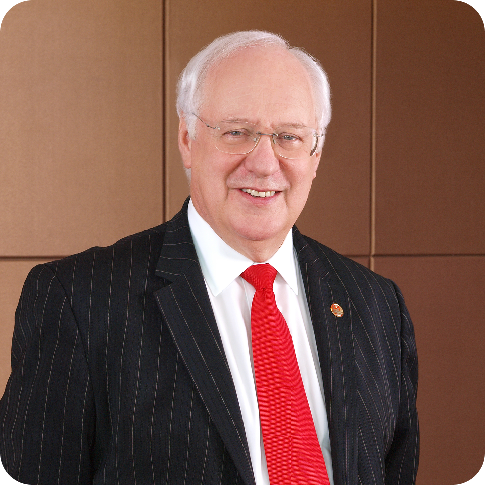 Man in suit and red tie smiles, posing in front of a brown wall.
