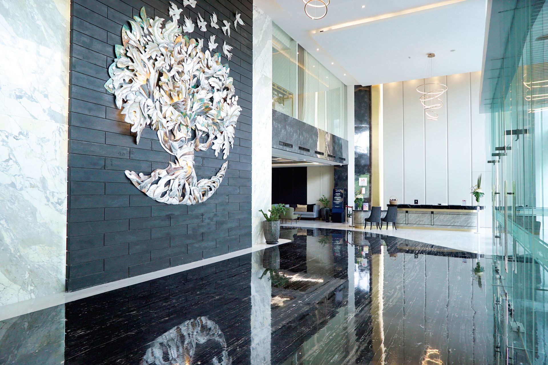 Lobby with a large tree art piece on a black wall, mirrored black floor, and glass windows.
