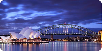 The sydney harbor bridge and opera house are lit up at night.