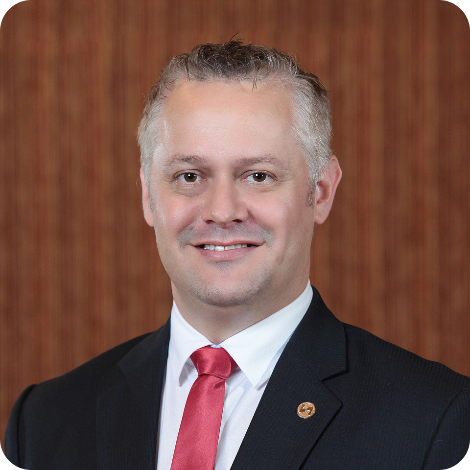 Man in suit and red tie smiles, set against a wooden background.