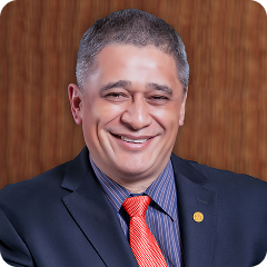 Man in suit and tie smiling, with a wooden background.