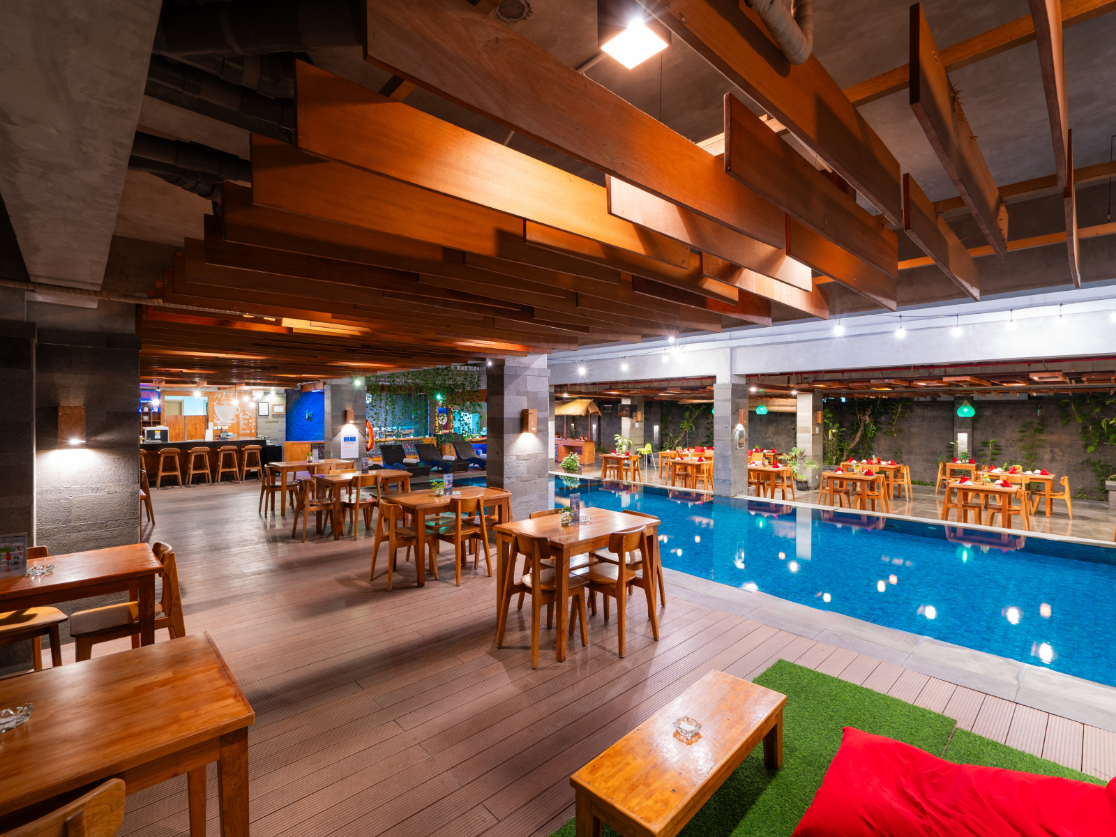 Restaurant with wooden tables, bar, and pool. Dark wood ceiling beams and seating around the pool.