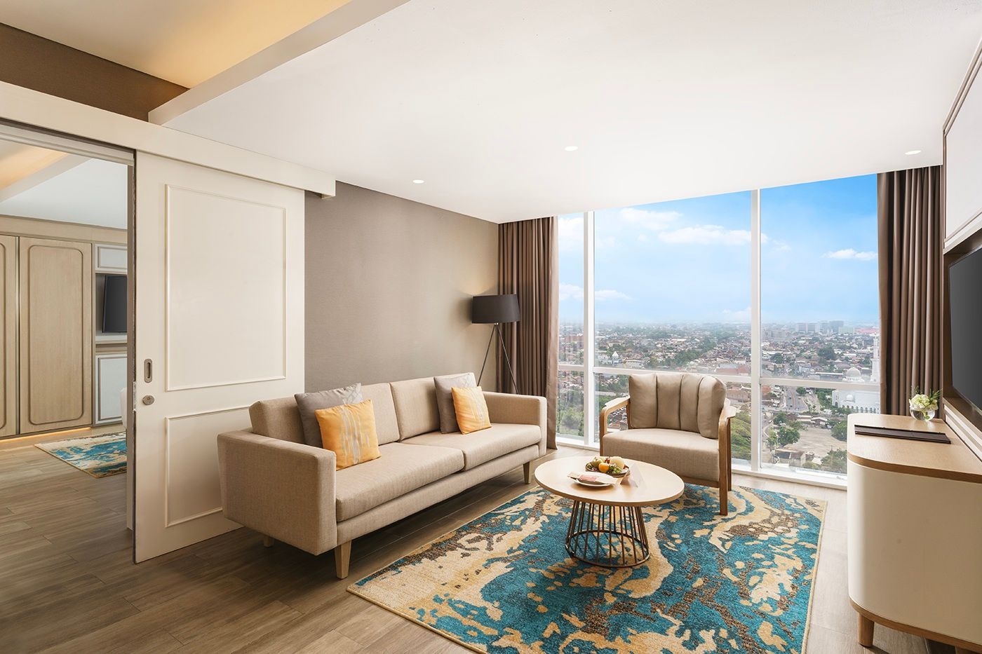Living room with a sofa, armchair, and a city view through a large window.