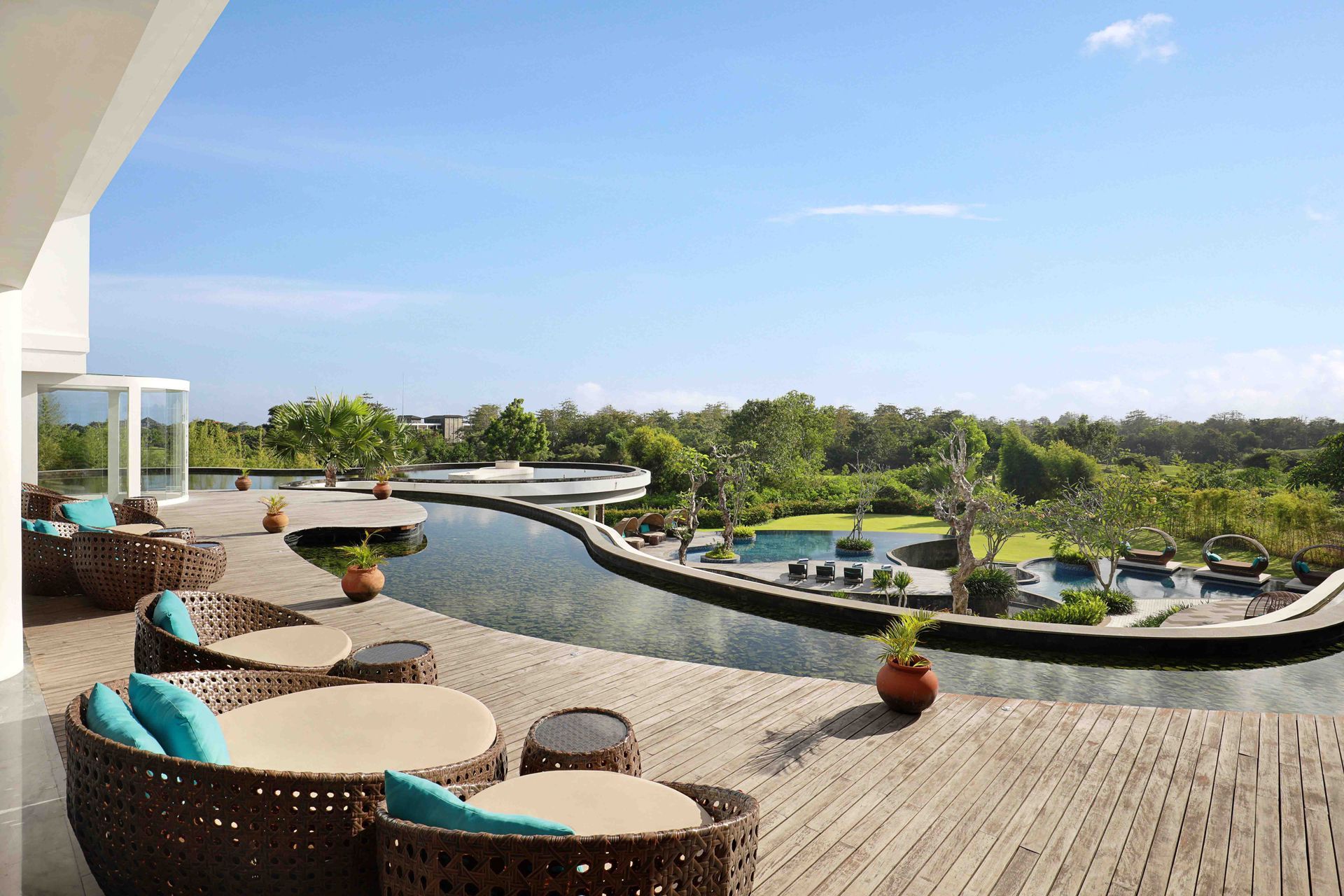 Terrace with wicker seating, overlooking a lagoon-style pool and lush greenery under a clear blue sky.