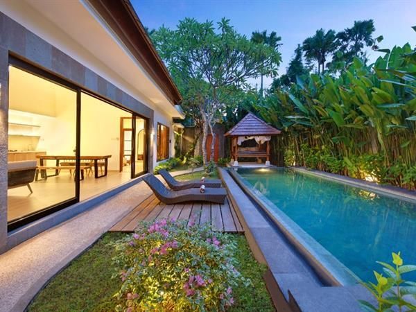 Luxury villa with a pool, lounge chairs, and a gazebo, surrounded by lush greenery at dusk.