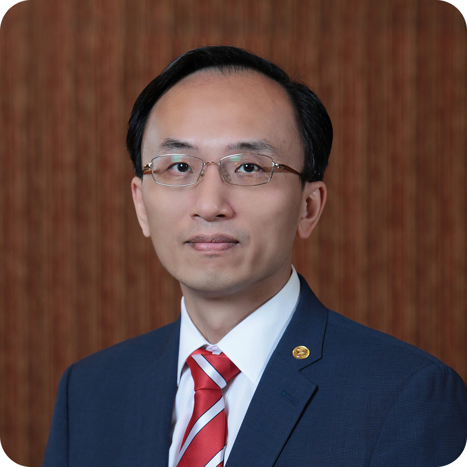 Man in suit, glasses, and red tie, smiling slightly, in front of a wooden backdrop.